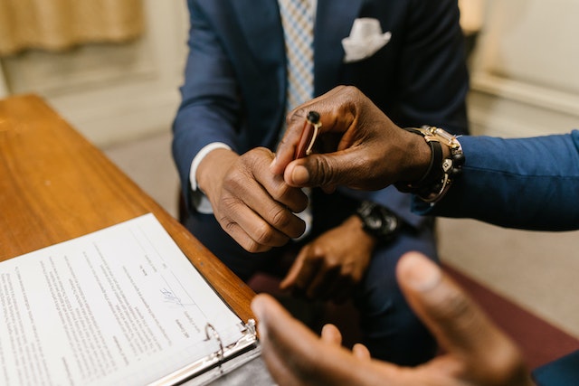 One person reaching across a desk to hand a pen to another person